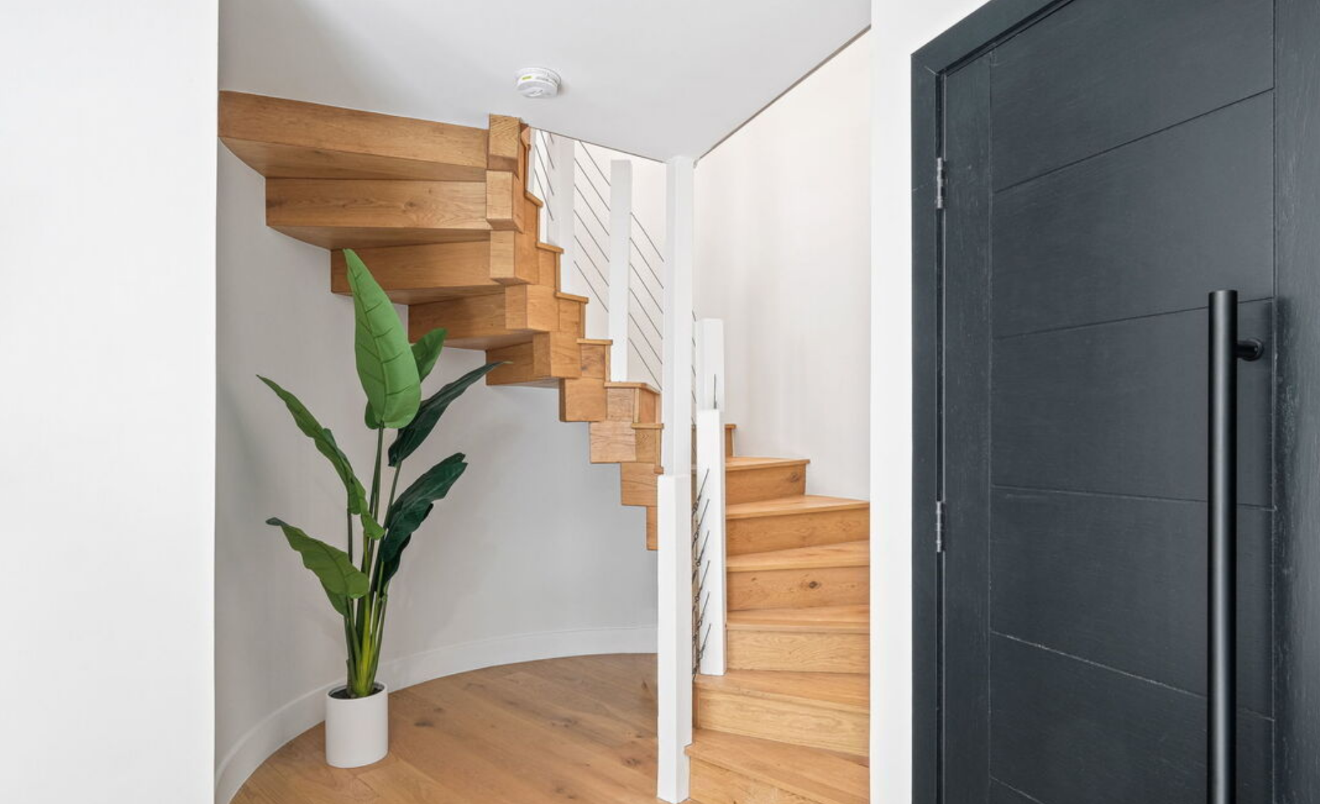 Floating white oak staircase against a curved plaster wall